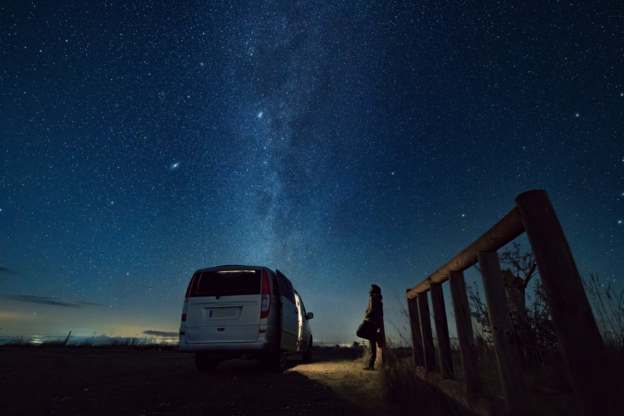 Man looking up to the night sky, riddled by stars. 