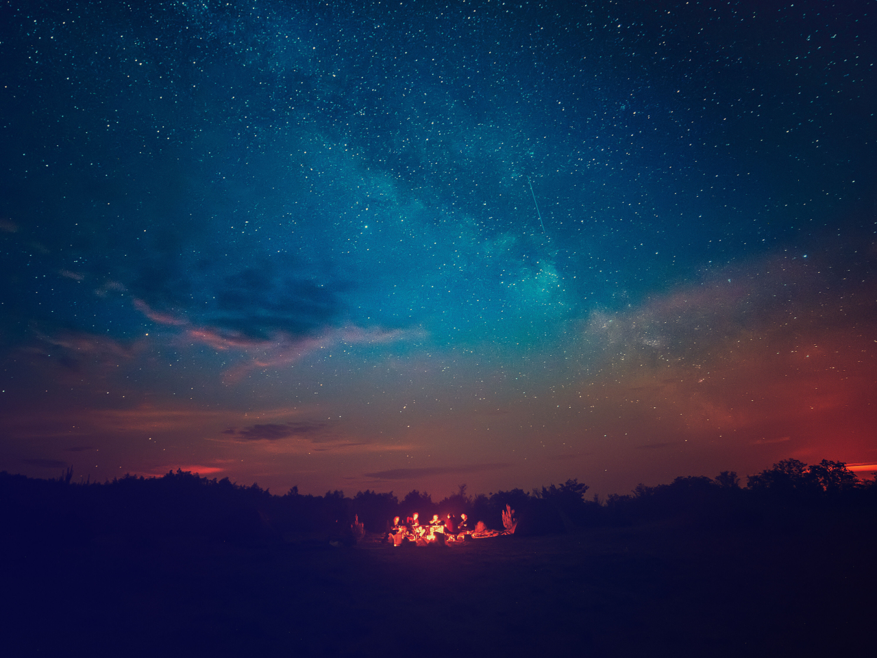A photo of people near a camp fire under a starry night sky. 