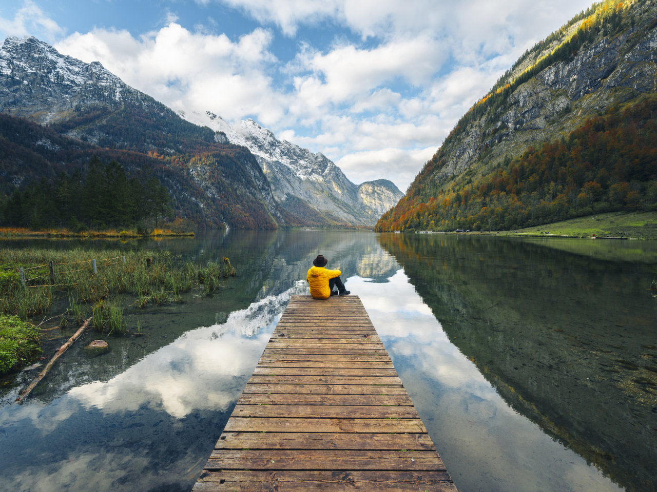 A man sitting at the end of a dock overlooking mountains. 