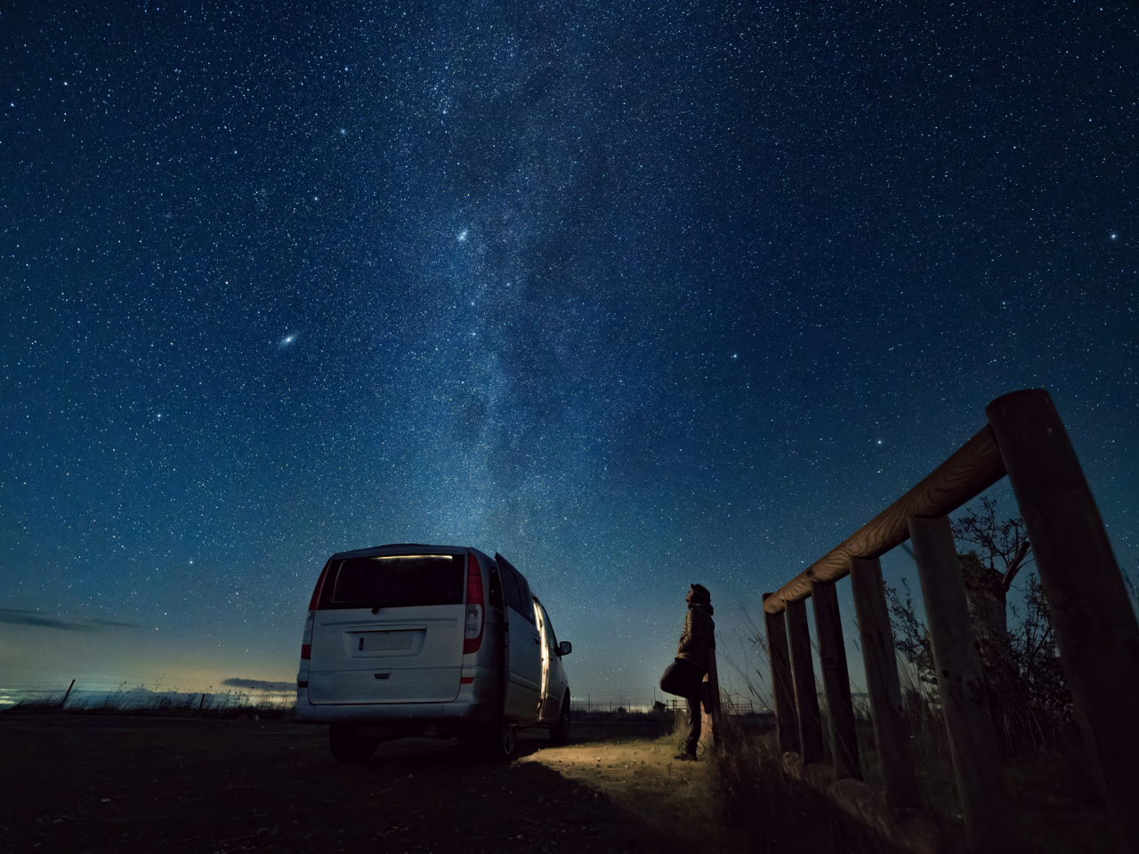 Man looking up to the night sky, riddled by stars. 