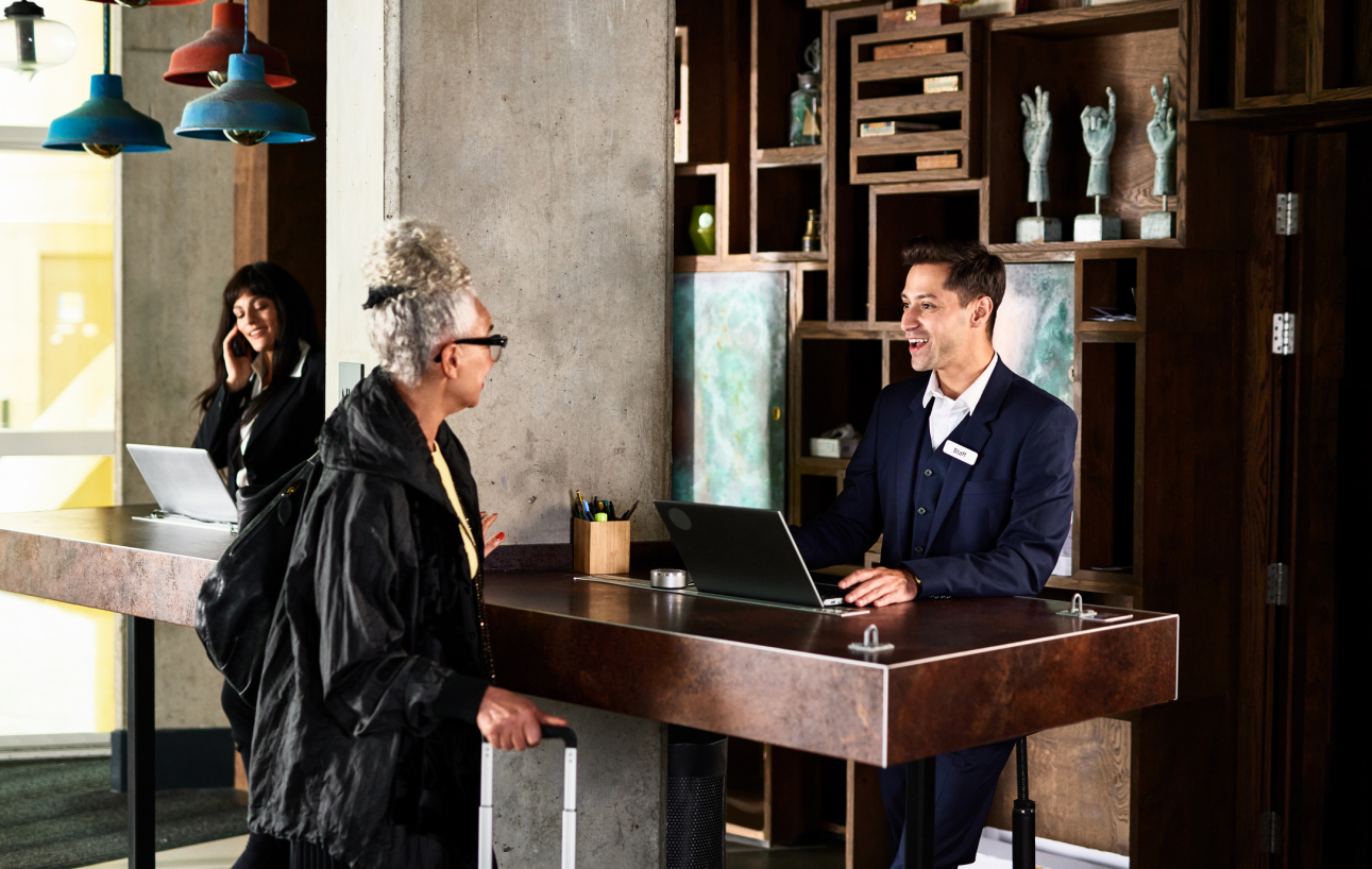 Younger hotel attendant checking in an older woman. 