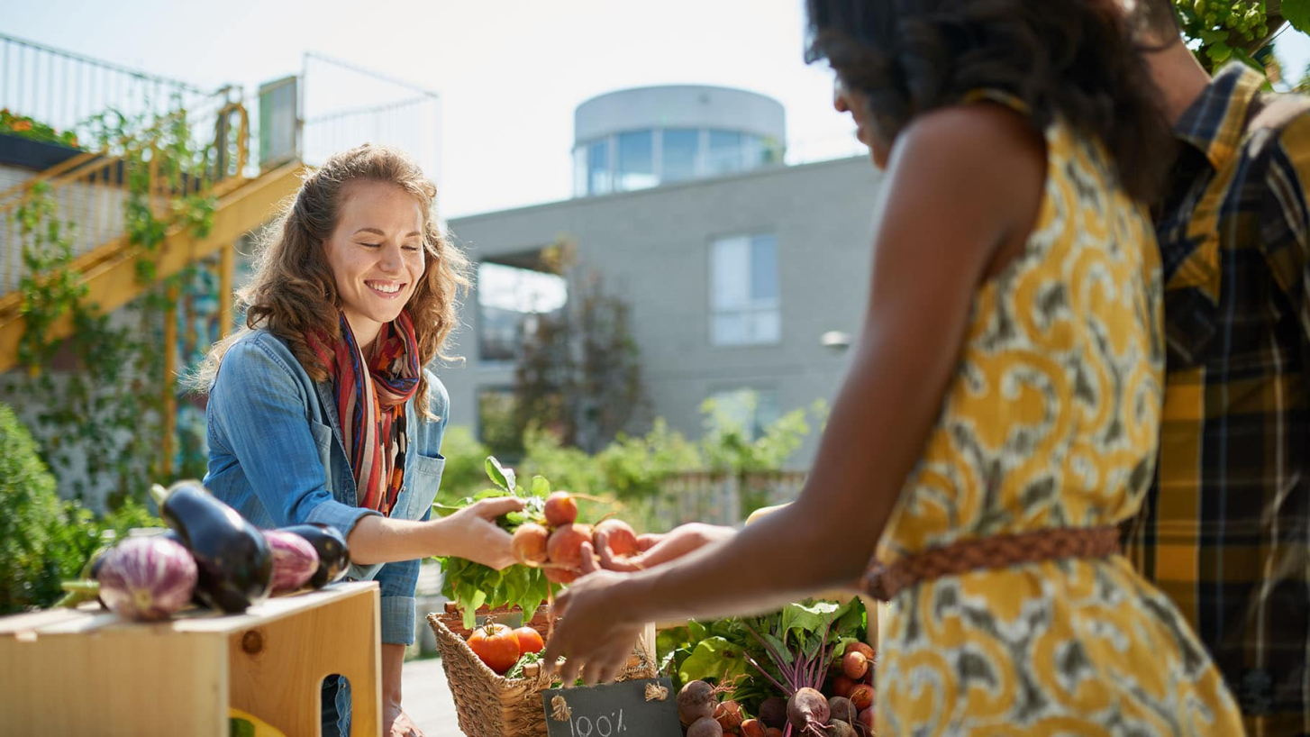 A photo of a woman handing fruits to a couple. 