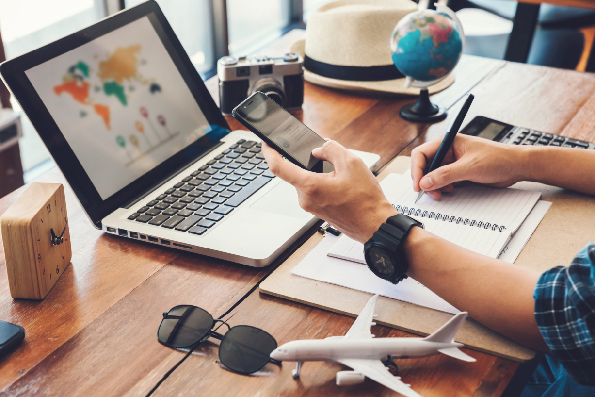 A photo of someone planning travel on their phone and laptop. 