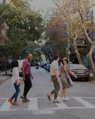 four people walking across a street lined with trees and cars