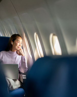 A photo of a woman on a laptop. She's looking outside the airplane window. 