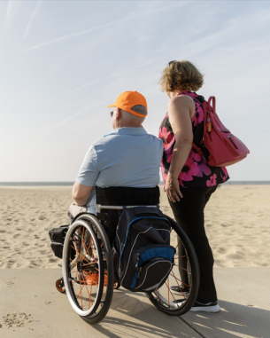 A couple looking at the beach, with one of them in a wheelchair. 