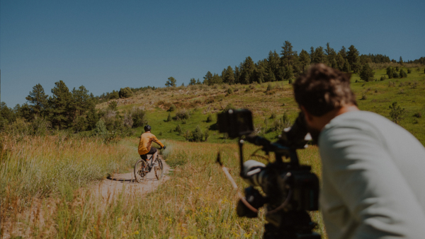 A man taking a video of someone on a bicycle on a dirt path 