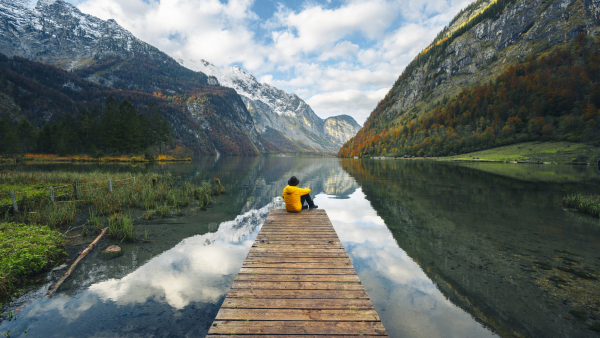 A man sitting at the end of a dock overlooking mountains. 