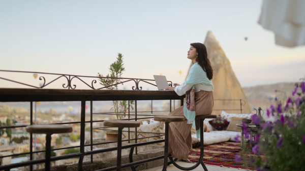 A photo of a woman sitting on a balcony searching through her laptop. 