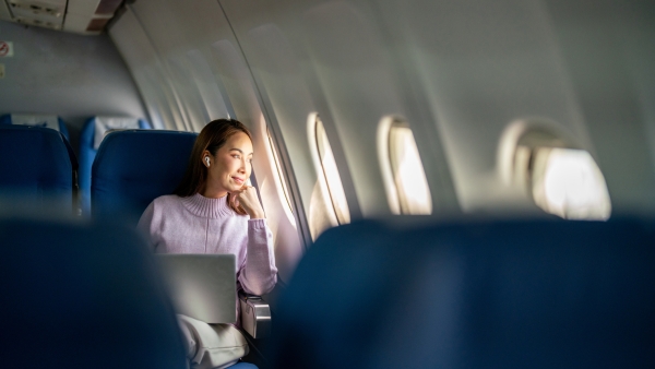 A photo of a woman on a laptop. She's looking outside the airplane window.