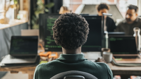 A photo of a curly-headed man sitting in front of a computer. 