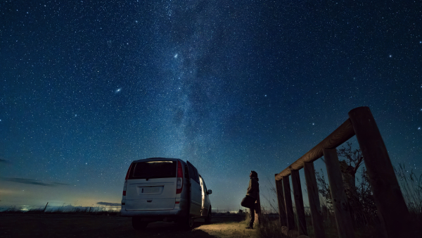 Man looking up to the night sky, riddled by stars. 
