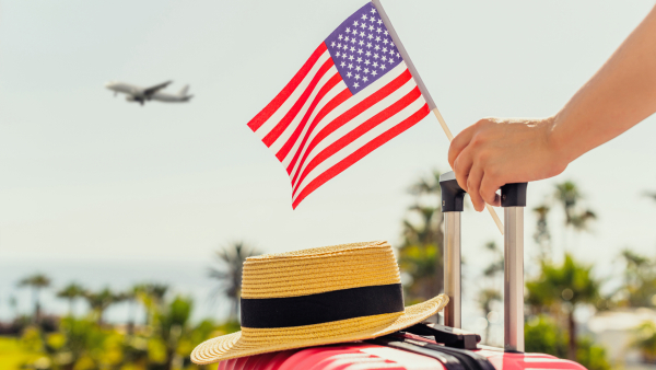 A traveler holding their luggage along with an American flag. 