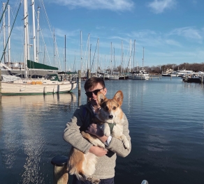 August Erickson holding a dog with sailboats in the background in Annapolis, MD