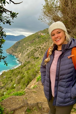 Alyssa Patton on a cliffside trail in Italy, with bright-bluish turquoise ocean in the background