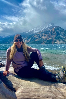 Alyssa Patton seated on a rock in front of a lake in Wyoming, with snow-dusted mountains in the background