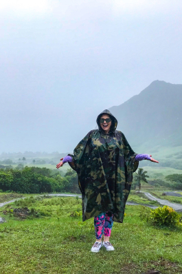 Angela Vaughn wearing a rain poncho ins a rainy/misty field with mountains in the background