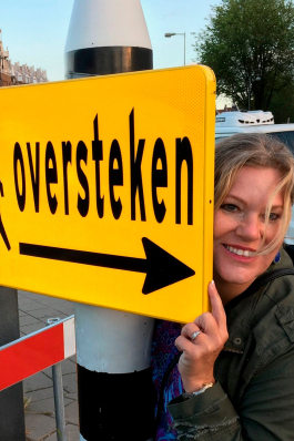 Angie Austin peeking our from behind a sign in Dutch that says "oversteken"