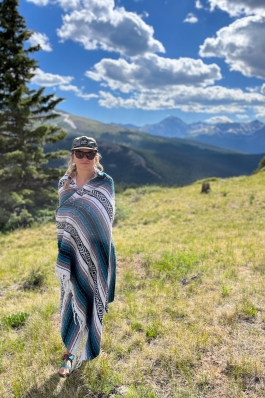Mattie Hall stands wrapped in a woven blanket on a grassy hillside in BreckenridgeCO