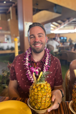 Steve Vaughn in Hawaii wearing a lei with a pineapple beverage in front of him