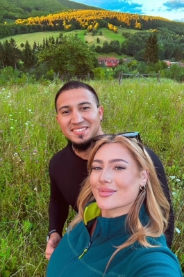 A photo of Larisa and her partner standing in a grassy plain. 