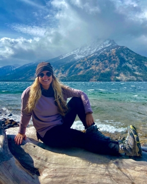 Alyssa Patton seated on a rock in front of a lake in Wyoming, with snow-dusted mountains in the background