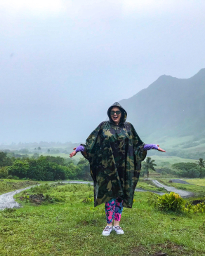 Angela Vaughn wearing a rain poncho ins a rainy/misty field with mountains in the background