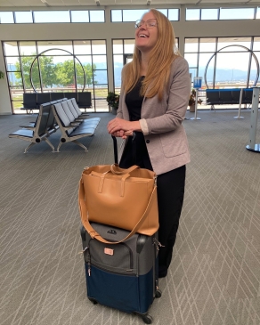 Laura Libby laughs while holding her carryon luggage in an airport