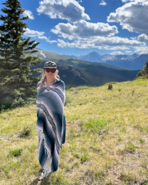 Mattie Hall stands wrapped in a woven blanket on a grassy hillside in BreckenridgeCO