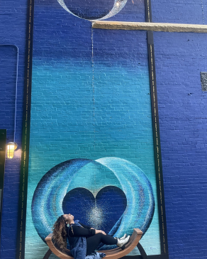 A photo of Melanie sitting on a beach underneath a mural