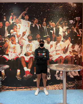 A picture of Andy in front of a pictured wall of Miami Heat players
