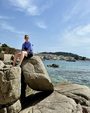 A photo of Dylan sitting on a rock overlooking the sea