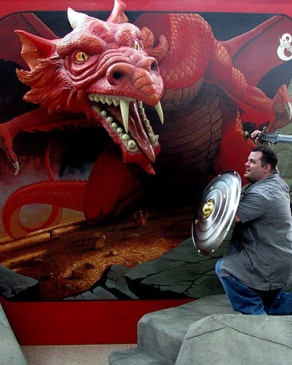 A photo of Eddie with a sword and shield looking at a cardboard dragon