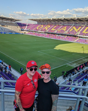A photo of Lori and her partner with the Orlando City SC field in the background.