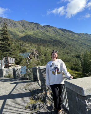 Eve standing on a viewpoint, with a picturesque view of Anchorage's mountains. 
