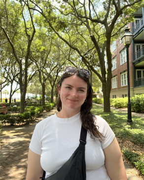Eve smiling in front of trees on a trail. 