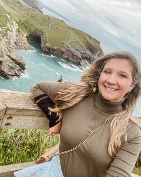 Alexis smiling on the edge of a cliff overlooking a body of water. 