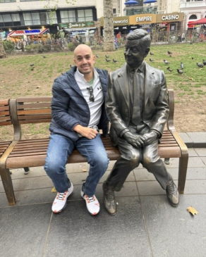 Mike takes a seat on a bench next to a statue in London. 